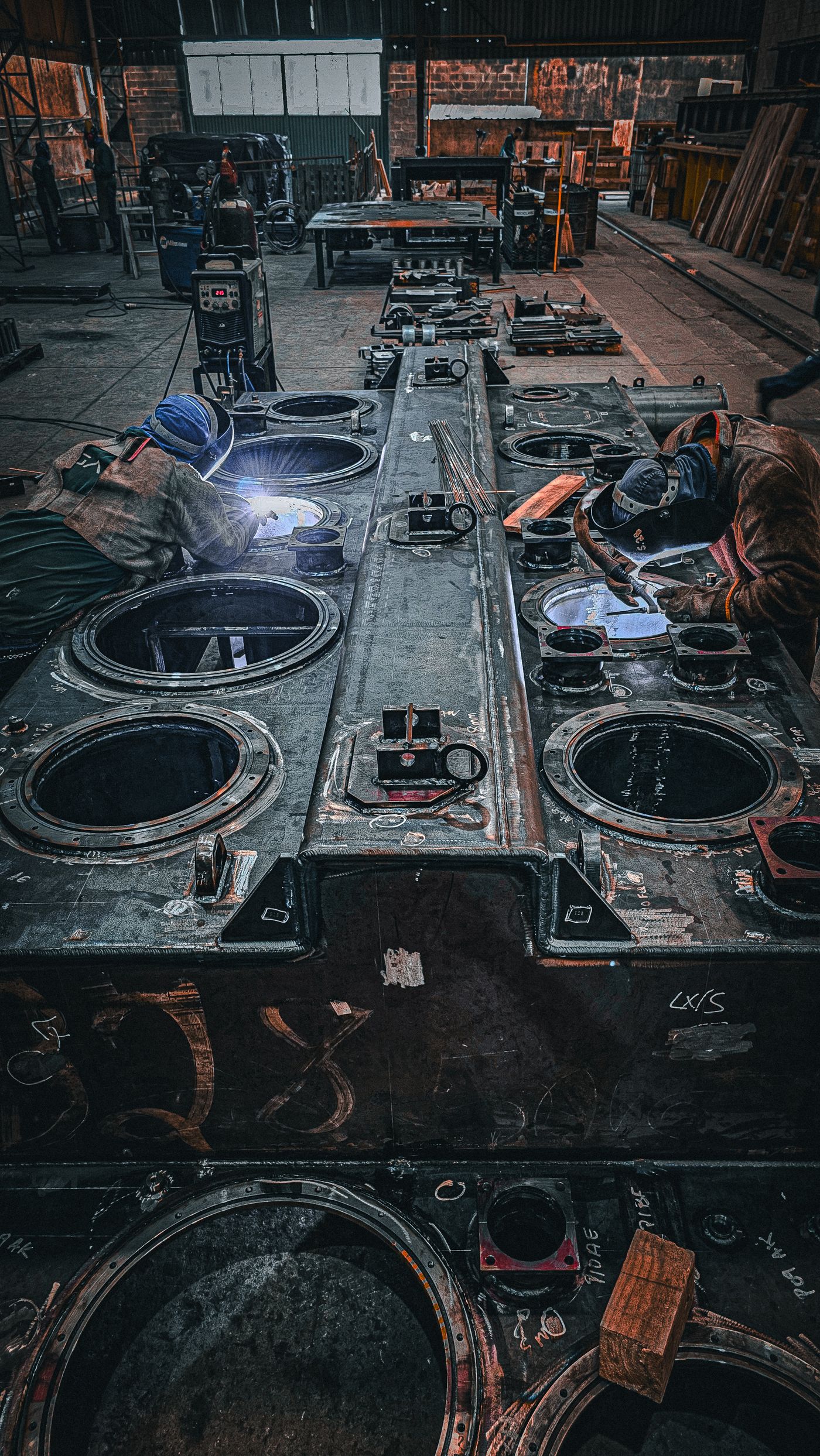Workers fabricating large steel plate assemblies in an industrial workshop